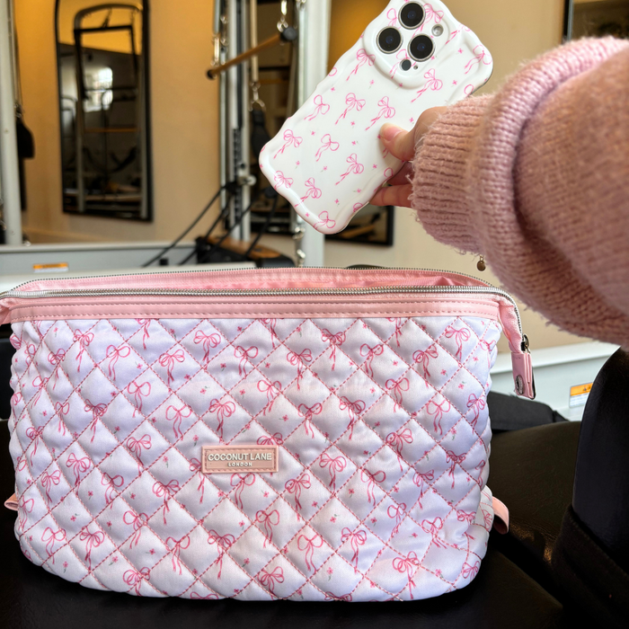 Hand holding a phone with a pink bow case above a quilted makeup bag featuring dainty bow pattern.