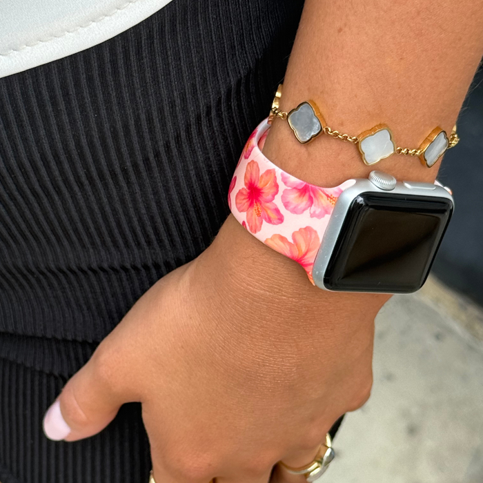 Pink hibiscus print Apple Watch strap paired with a gold bracelet featuring white stones on someones wrist.