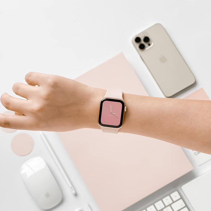 Powder pink Coconut Lane NAKD Apple Watch Strap worn on a hand, shown at a pastel desk with phone, keyboard, and mouse.