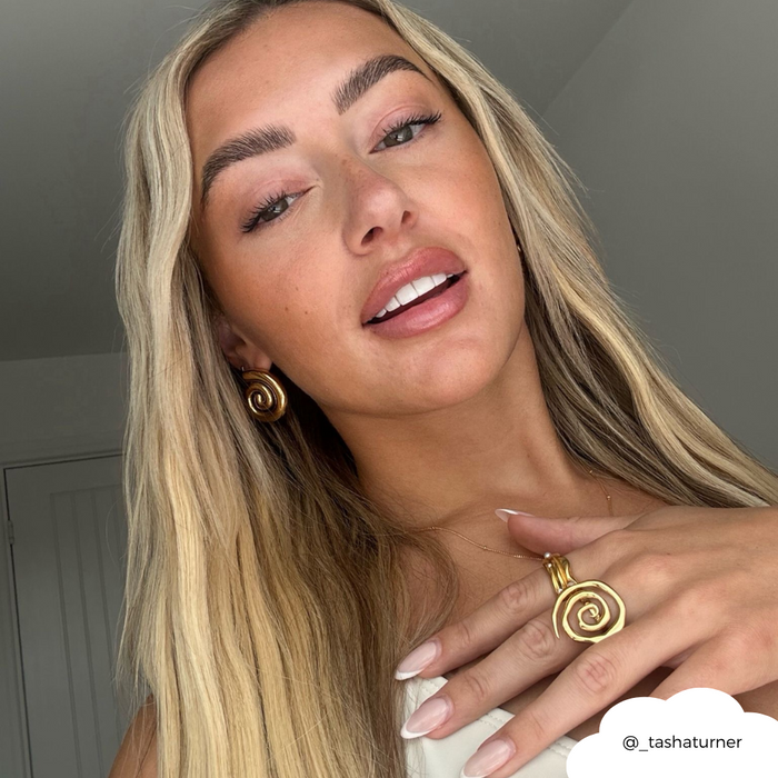 Smiling woman with long blonde hair wears gold Coconut Lane shell earrings, a matching gold shell necklace, and ring.