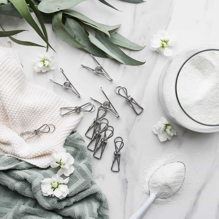 Ever eco clothes pegs styled with some textured towels on a marble surface with some laundry powder in a glass container & some decorative leaves & flowers.