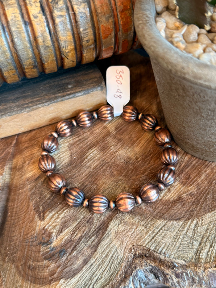 Copper ribbed pumpkin-bead bracelet on wood, elastic string visible between beads.