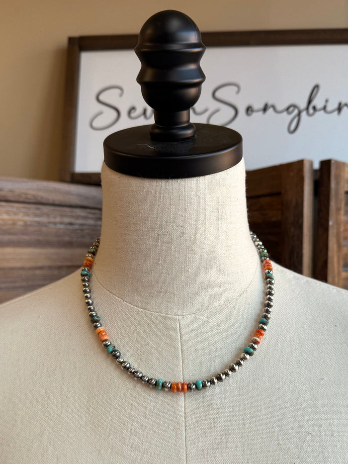 Beaded turquoise-and-orange necklace with metallic beadwork, centered on a mannequin bust