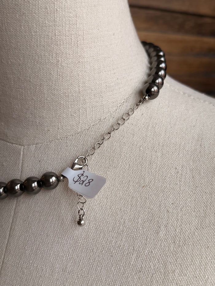 Silver pearl necklace clasp and tag on display, close-up of round beads