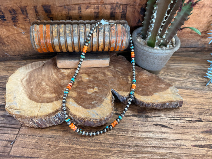 Turquoise and orange beaded necklace with a dark arrowhead-style centerpiece on wood