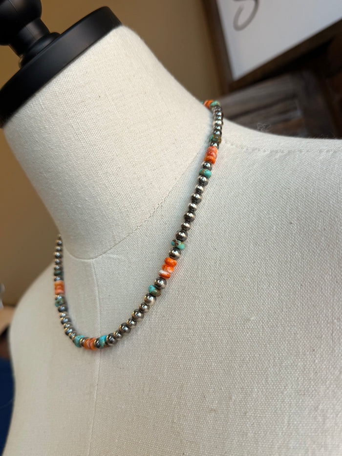 Turquoise and orange beaded necklace with a small dark center charm and metallic links
