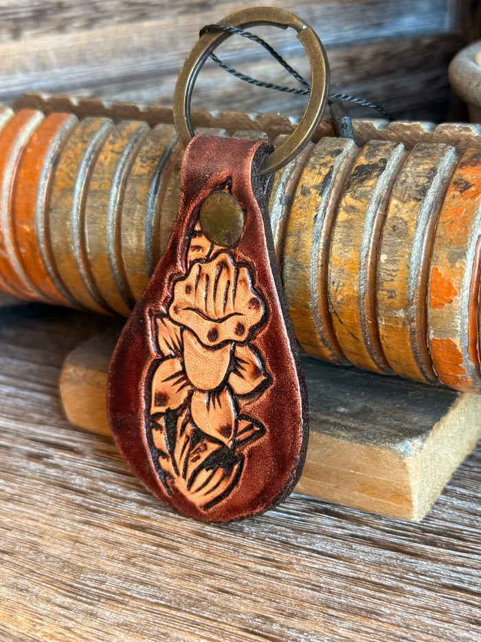 Brown tooled leather keychain with metal ring and embossed facial detail, teardrop shape