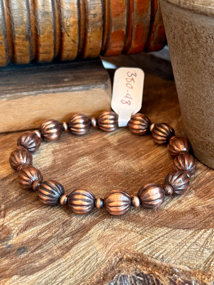 Copper stretchy bracelet with ribbed pumpkin beads, close-up on wooden surface.