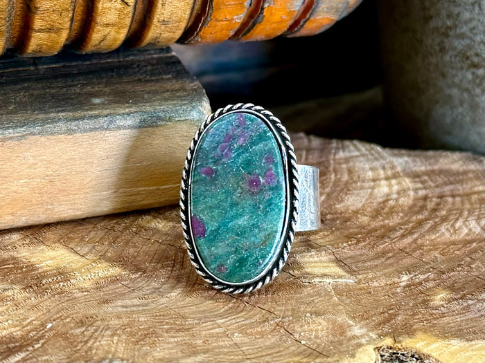 Turquoise oval stone ring with silver rope border and adjustable band, close-up.