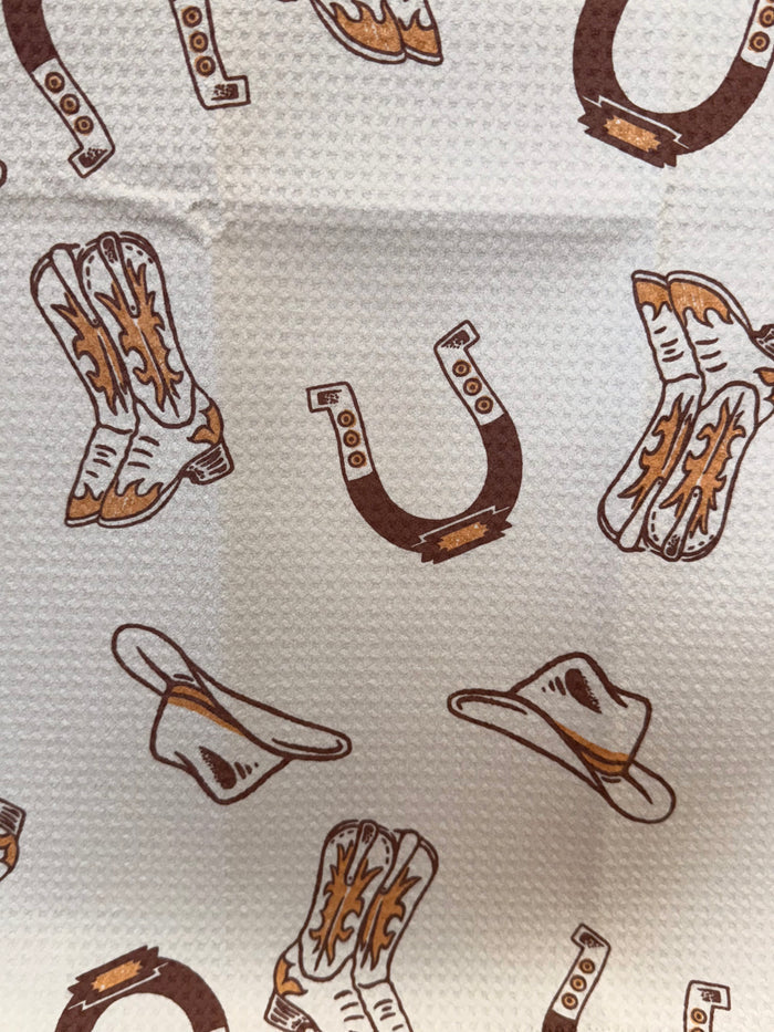 Cowboy boots and hats towel with repeating western print pattern in brown and orange