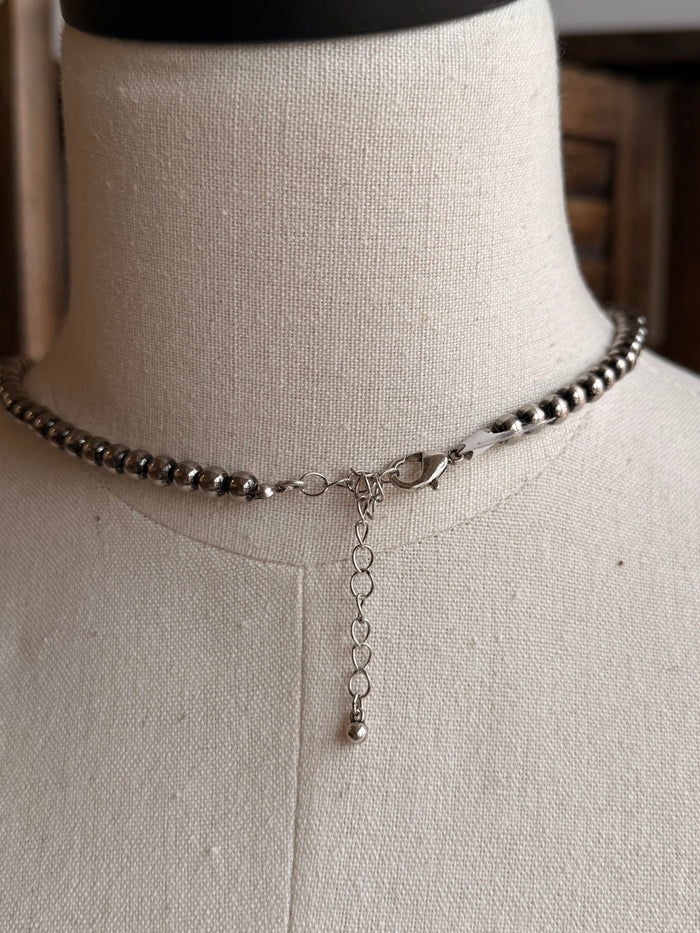 Graduated silver pearl necklace detail: bead chain with small dangling charm