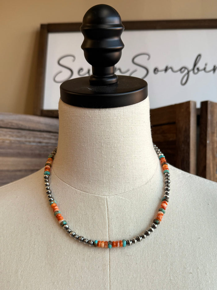 Turquoise and orange bead necklace centered on white mannequin with dark round metal beads