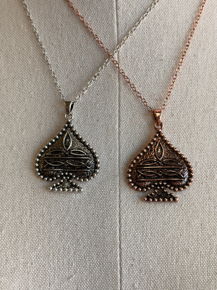 Spade charm necklaces close-up: silver and copper teardrop pendants with textured detailing