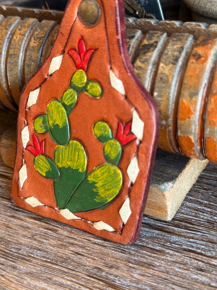 Close view of orange leather cactus keychain with painted green cactus and red flowers.