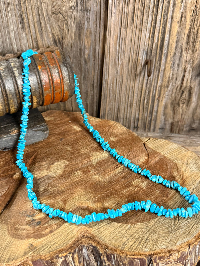Turquoise chip bead necklace shown coiled on a round wooden slab