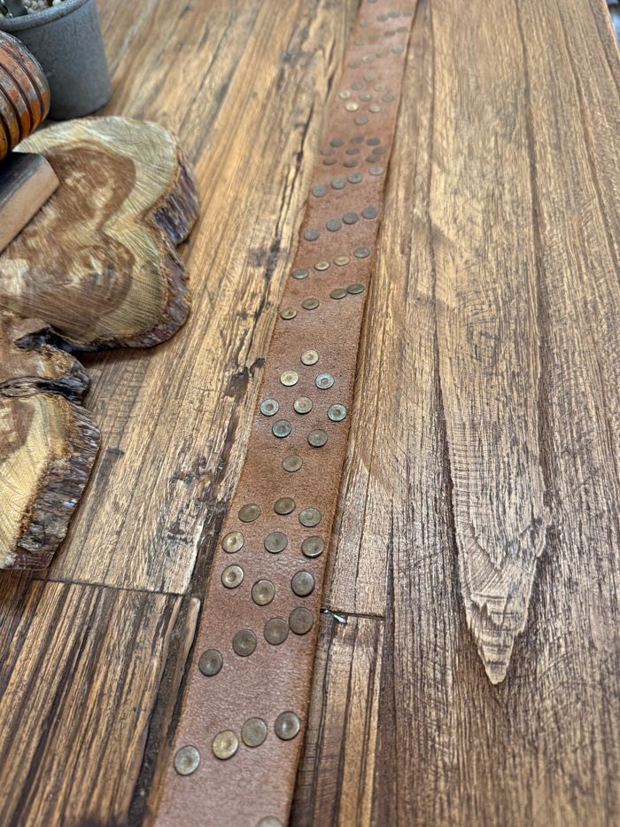 Brown leather strap detail with spaced round brass studs along center strip