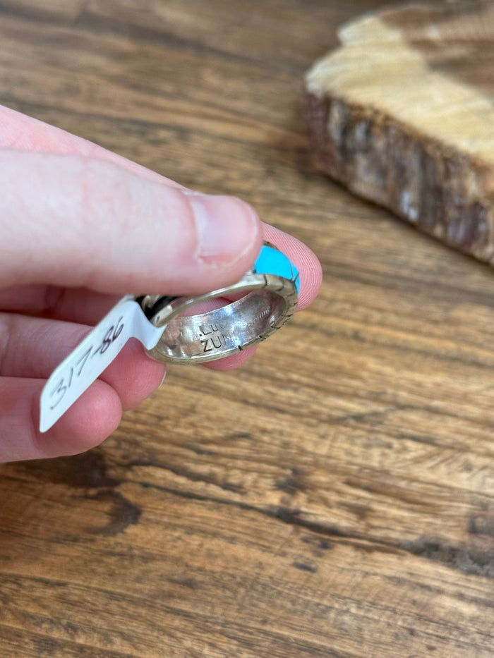 Turquoise inlay ring held by hand; silver band with blue stone row