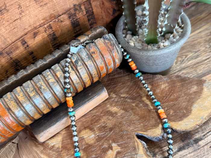 Turquoise and orange beaded necklace with dark centerpiece charm laid on wooden discs