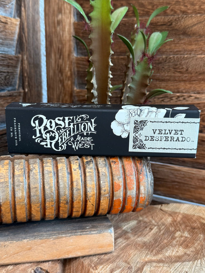 Velvet Desperado roll-on perfume oil box with ornate logo, beside orange roll holder