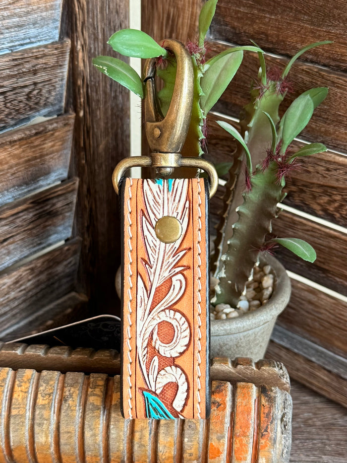 Tooled leather keychain close-up, orange strap with carved leaf pattern and feather charm