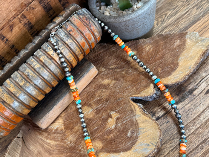 Turquoise and orange bead necklace draped across wood display, dark metal bead chain
