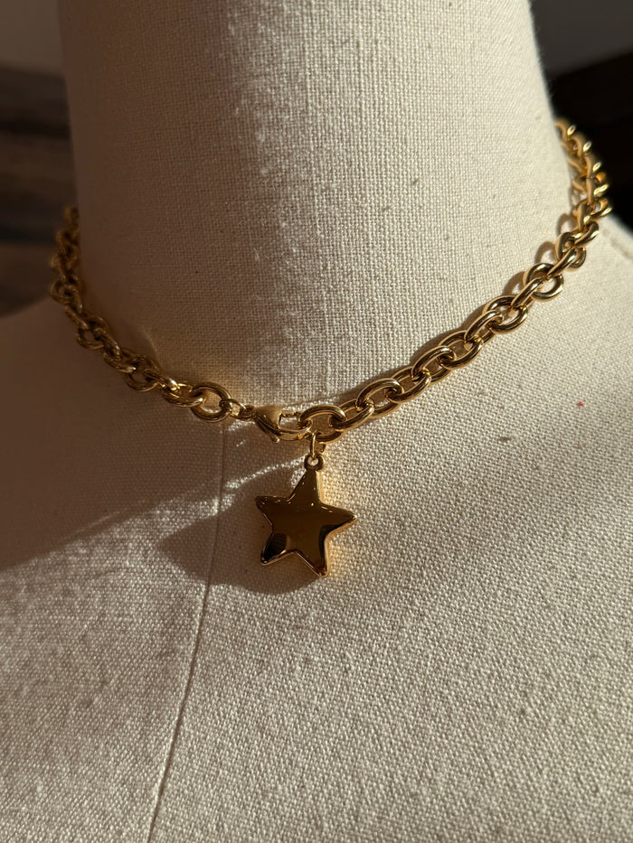 Gold chain necklace with small star charm, close-up of curb links