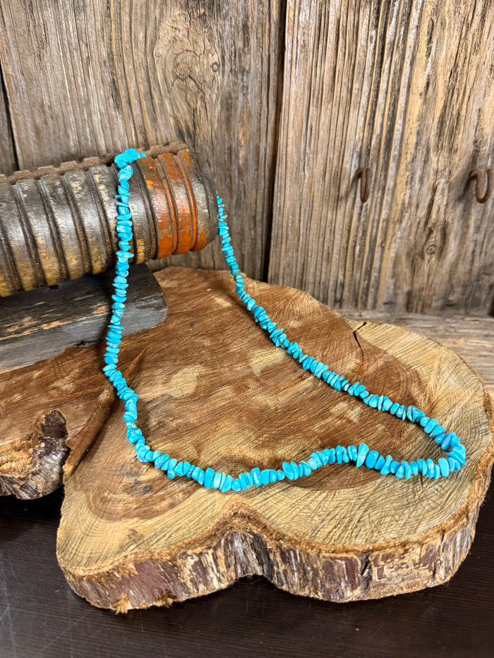 Turquoise chip bead necklace, strung beads in a U-shape on wood slab