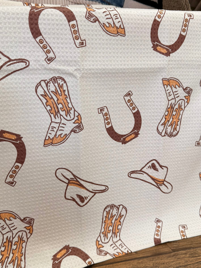 White cowboy boots and hats towel with brown and orange western icons, close-up
