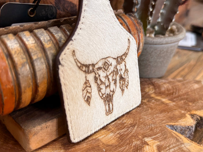 Cow skull hair-on key fob close-up: gold-tone skull and feather details on white patch
