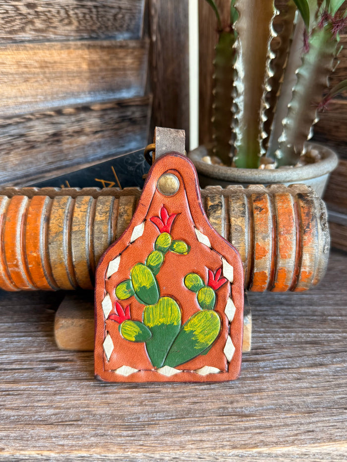 Leather cactus keychain with painted green cactus and red flowers on orange.