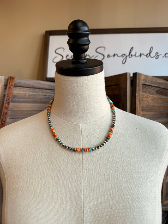 Turquoise and orange bead necklace on white mannequin bust with dark metal bead strand