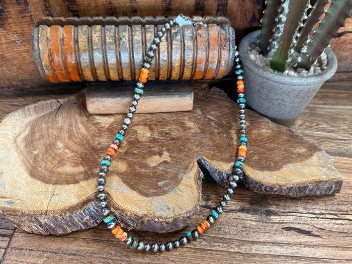 Turquoise and orange beaded necklace featuring a dark centerpiece charm and metal bead strand