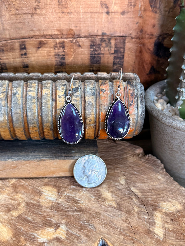 Silver fishhook amethyst earrings with purple teardrop stones, coin shown for scale