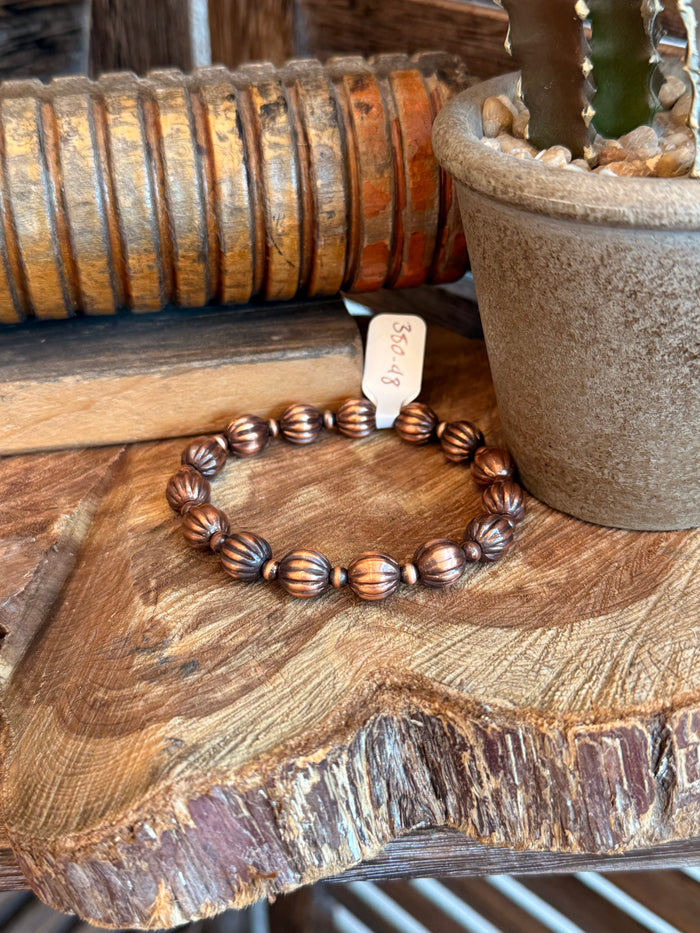 Genuine copper stretchy bracelet with ribbed pumpkin beads, on wood.