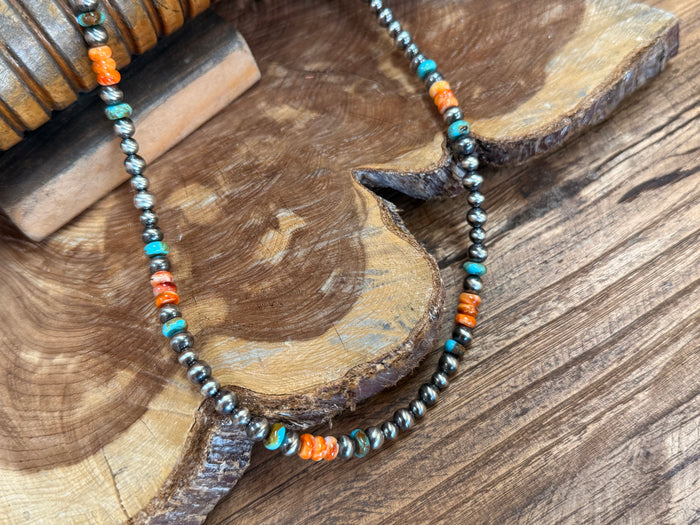 Close-up of turquoise, orange, and metallic beads with a dark centerpiece charm