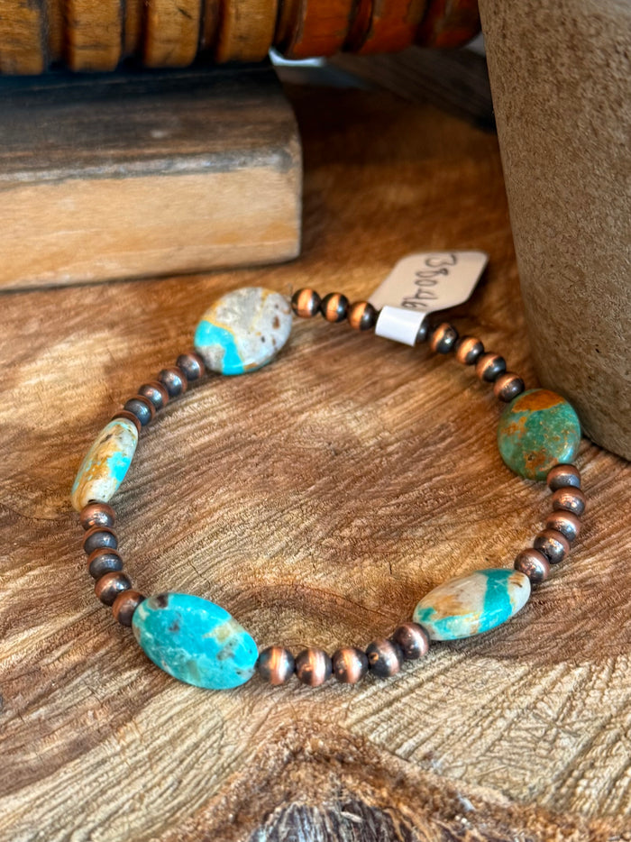 Copper stretchy bracelet with oval turquoise beads and dark round spacer beads.