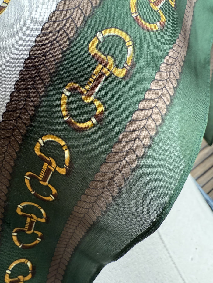 Green scarf close-up with gold snaffle bit print and dark green braided border