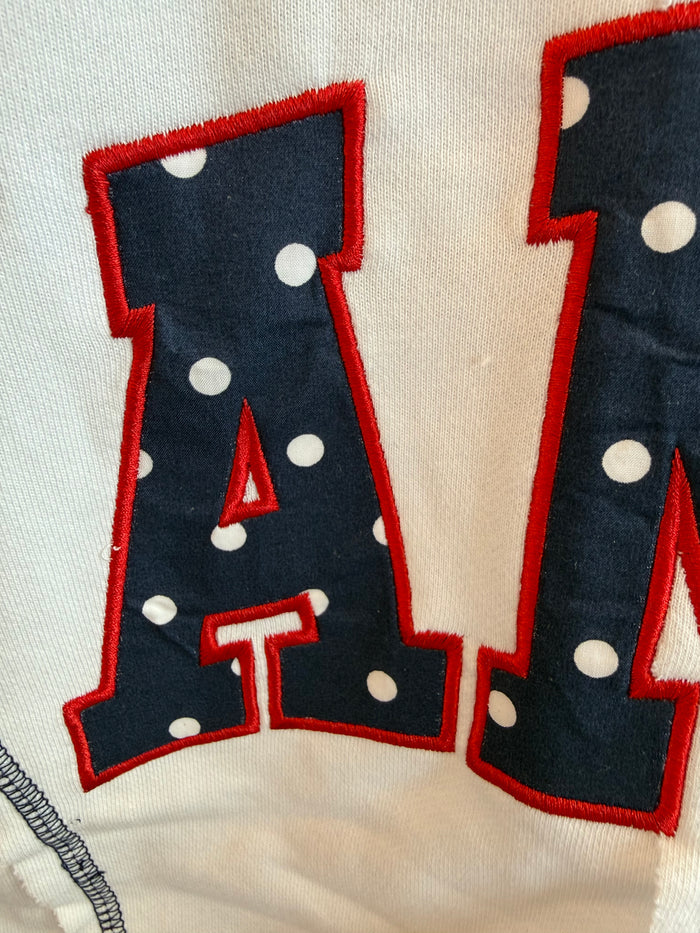 Cream short-sleeve sweatshirt with embroidered navy letter shapes outlined in red