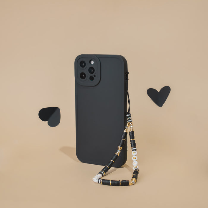 Black smartphone with a black and gold beaded phone strap, standing upright on a beige background.
