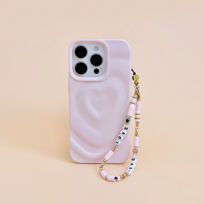 Pink phone case with Coconut Lanes pastel beaded phone strap on a light beige surface.