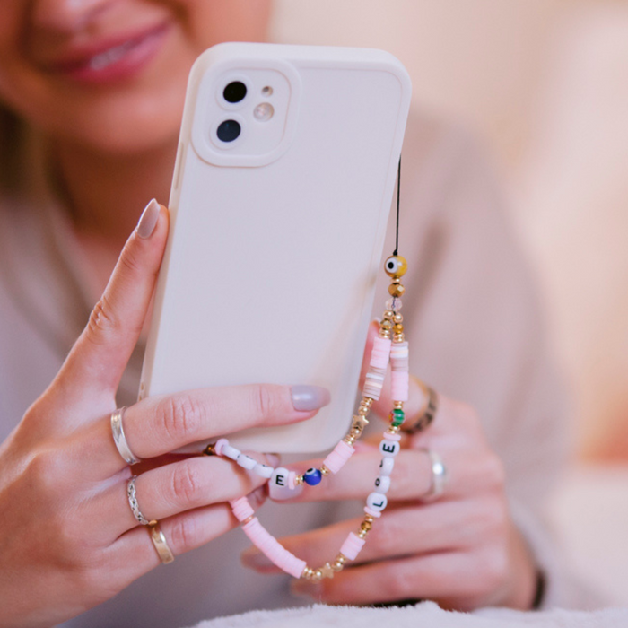 Woman holding a white phone with a colourful beaded Coconut Lane phone strap featuring heart-shaped beads.
