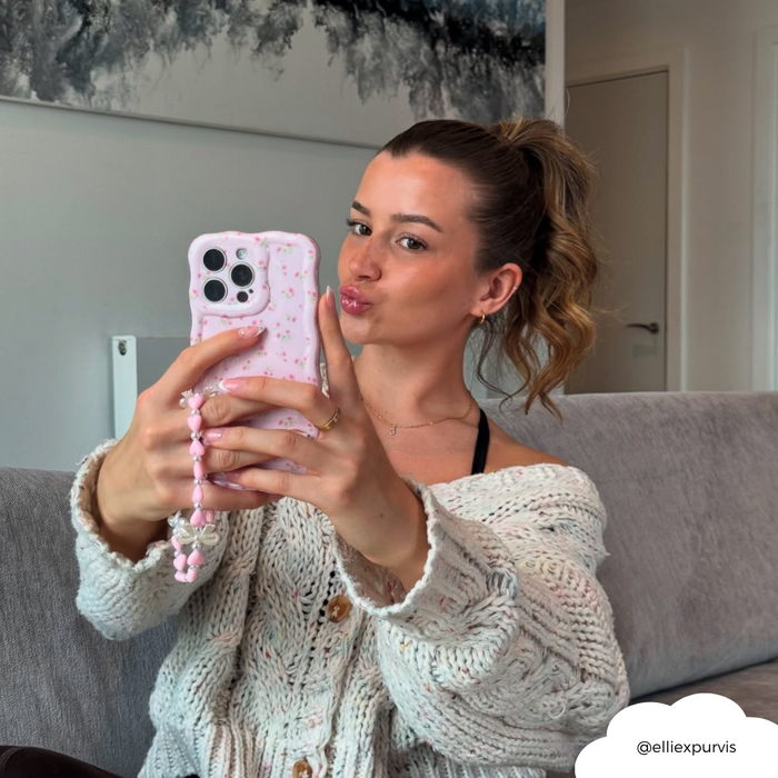 Woman on a couch taking a selfie with a pink phone case and Coconut Lane’s Hearts & Bows patterned strap.