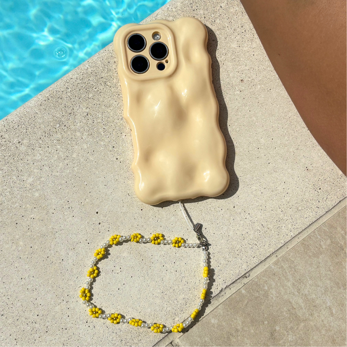 Phone with a beige wavy case and sunflower beaded strap beside a pool.