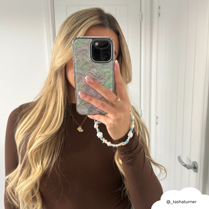 Woman with long blonde hair in mirror selfie, phone has Coconut Lane blue and pearl beaded phone strap.