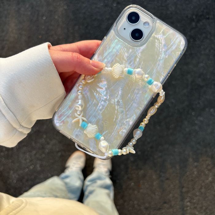 Hand holding phone with Coconut Lanes colourful beaded strap; person in white top and blue jeans.