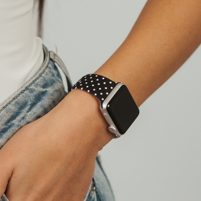 Woman in jeans and a white top wears a black Apple Watch strap with white polka dots from Coconut Lane.