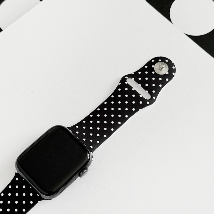 Black Apple Watch with Coconut Lane polka dot strap on a white geometric background.