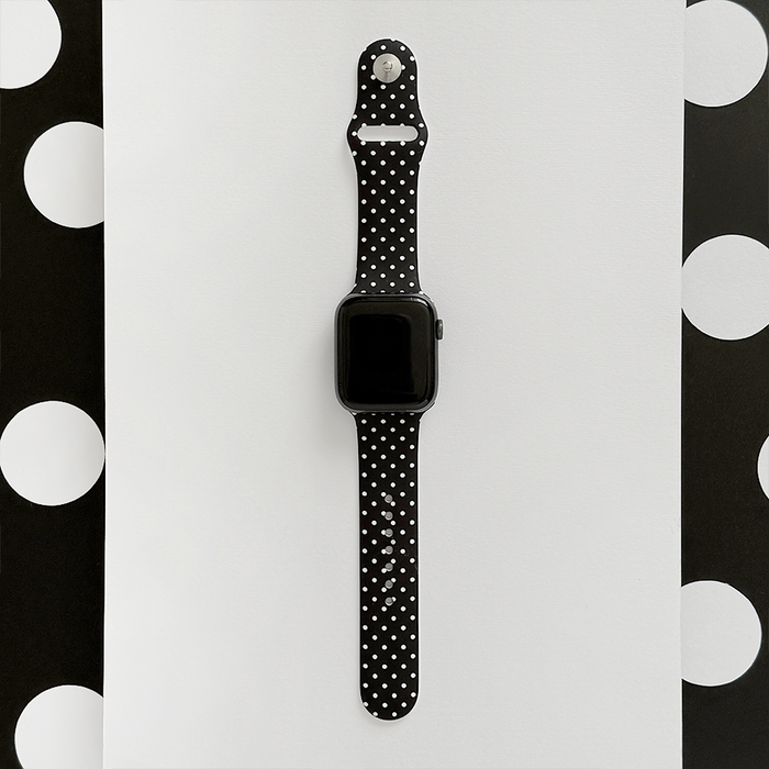Black polka dot Apple Watch strap by Coconut Lane displayed on white paper with a matching polka dot background.