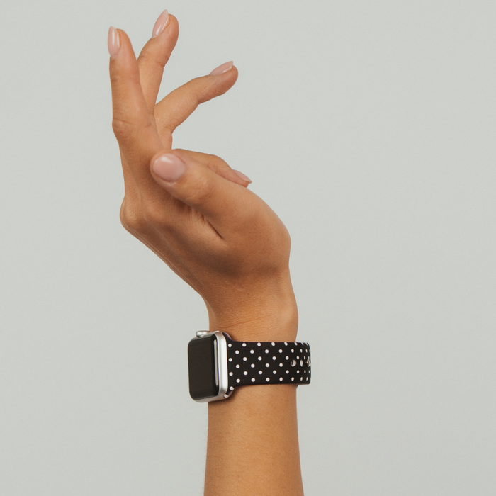 Black polka dot Apple Watch strap on a hand with manicured nails, shown against a light background.