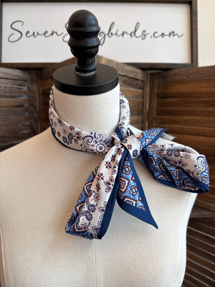 Blue paisley twilly scarf tied in a bow on a dress form, cream with navy and red accents